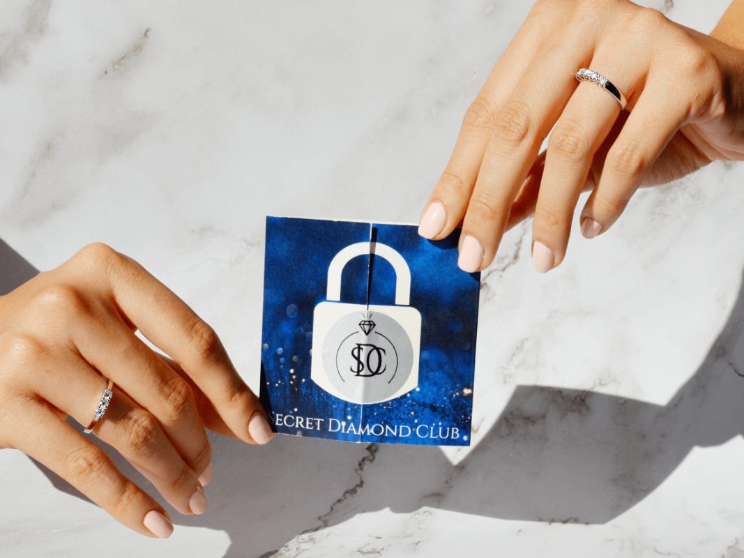 Две ръце държат картон с изображение на ключалка и логото на Secret Diamond Club.