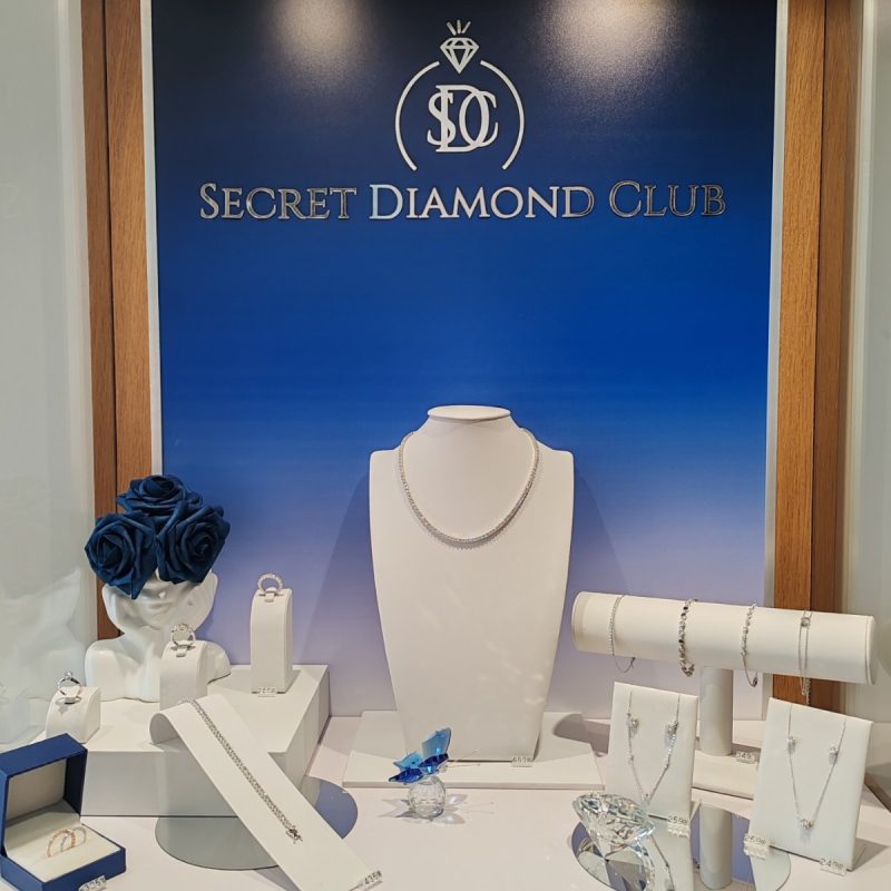 Бижута и аксесоари на дисплей с логото на Secret Diamond Club и син фон.