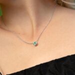 Сребърно колие със зелен мойсанит, носено на врата, с фокус върху камъка.